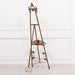 A 165cm tall French-style metal easel in antiqued gold finish with intricate details and an adjustable shelf.