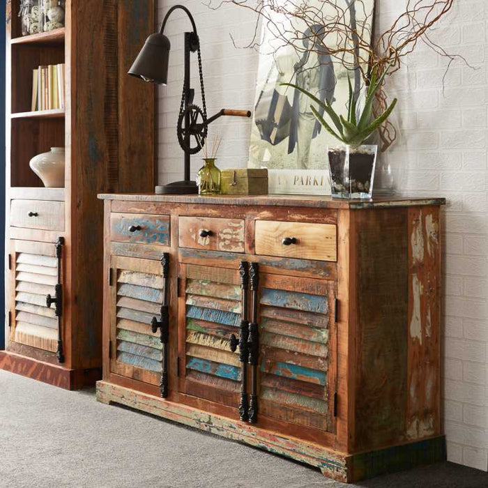 A large sideboard made of reclaimed wood with three drawers and multicolored panels, placed in a room with various decor.